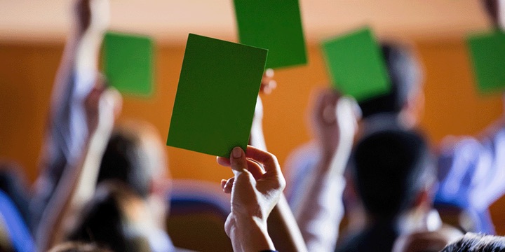 Hochgehaltene Hände in einer Versammlung, eine Hand hält eine grüne Karte